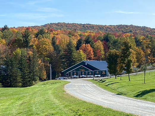 A beautiful autumnal photo of the Branon Family sugarhouse sounded by colorful maple trees