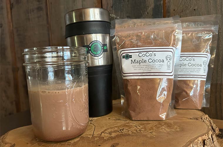 Photo of CoCo's Maple Cocoa with travel mug and mason jar on cut tree stump